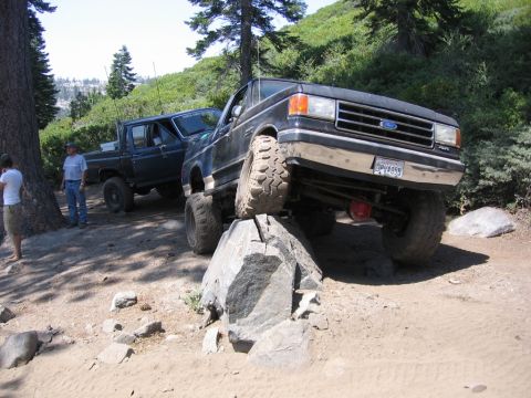1989 Ford Bronco - A black Ford truck navigates a rocky trail, with another truck visible behind it.