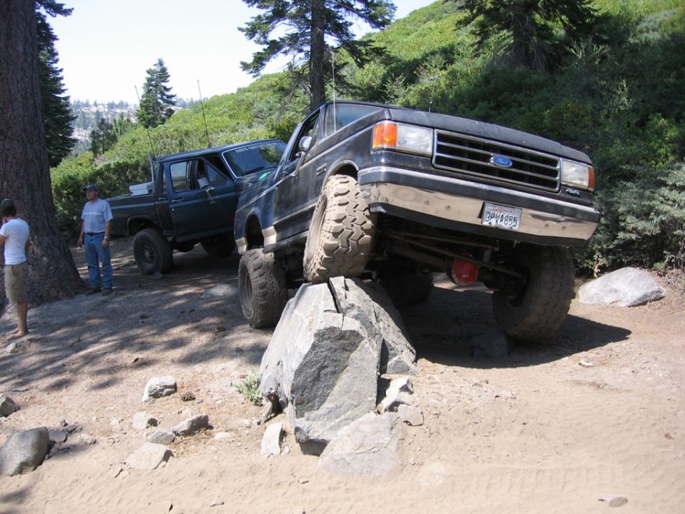 Black Ford truck with lifted suspension driving over rocks