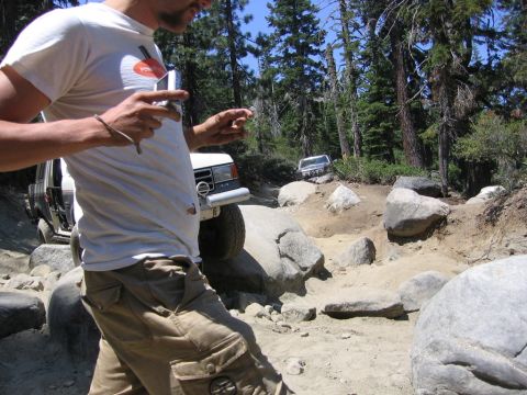 1989 Ford Bronco - Off-road vehicles traverse a challenging, boulder-strewn path through a forest.