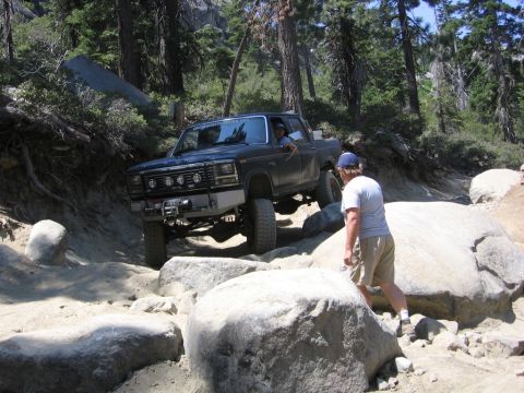 1989 Ford Bronco - A modified Ford pickup truck tackles a challenging off-road course with large boulders and trees.
