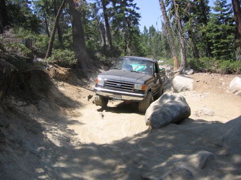 1989 Ford Bronco - A dark gray pickup truck navigates a rocky, wooded trail.