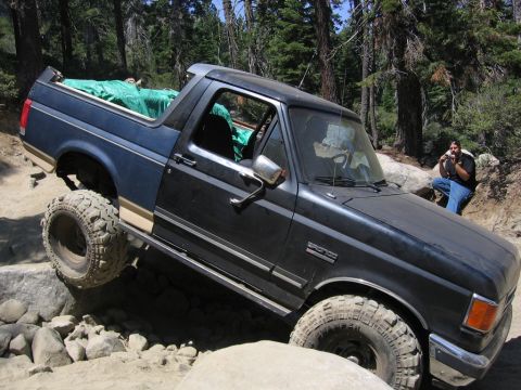 1989 Ford Bronco - A Ford Bronco navigates a rocky trail, with a person observing in the background.