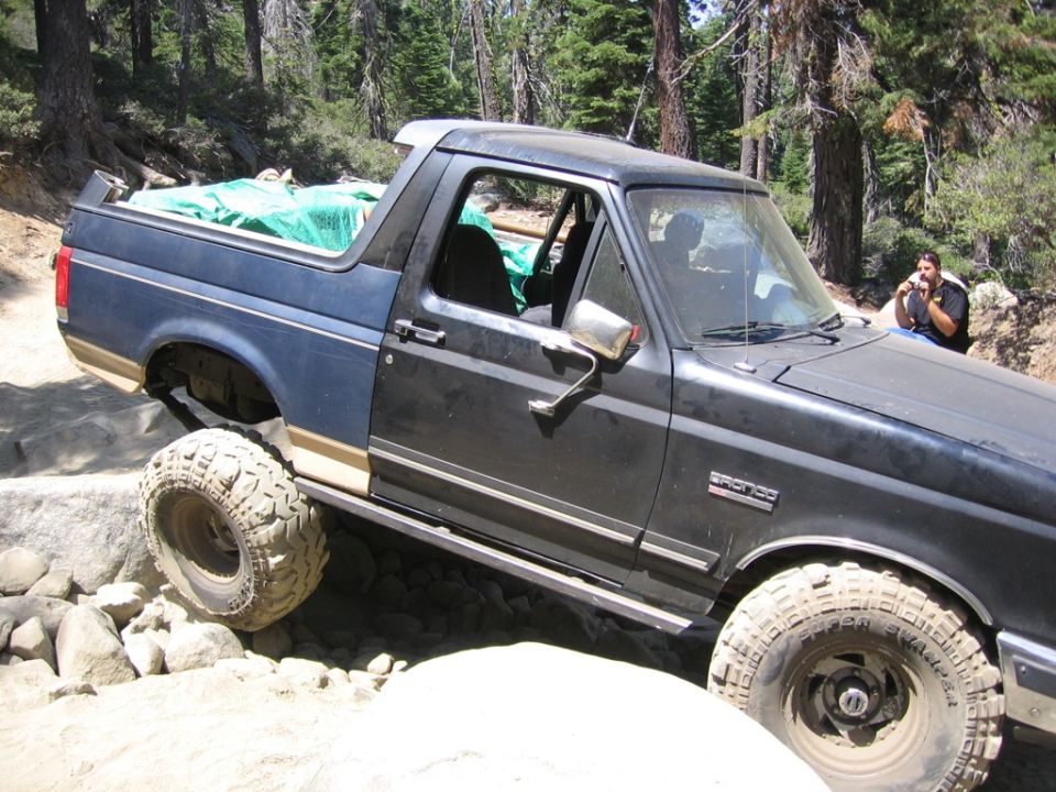 Blue and black 1989 Ford Bronco off-roading over rocks