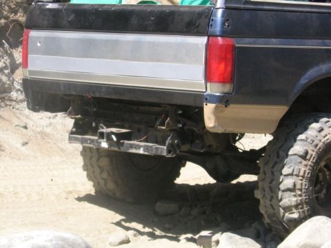 1989 Ford Bronco - The rear of a black Ford pickup truck is shown with large off-road tires, navigating a rocky terrain.