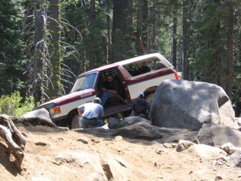 1989 Ford Bronco - 1989 Ford Bronco tackling a difficult off-road obstacle with assistance from onlookers.