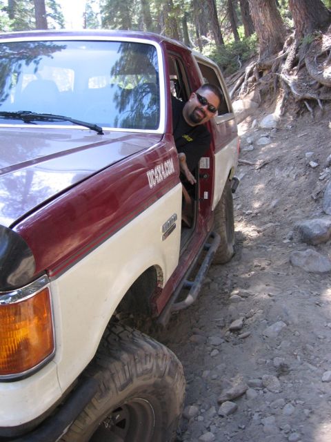 1989 Ford Bronco - A man poses in his two-tone Ford Bronco while off-roading on a rocky, wooded trail.
