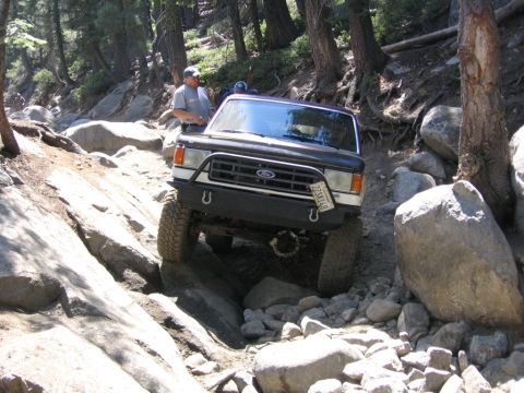 1989 Ford Bronco - This Ford Bronco is navigating a challenging rocky trail in a wooded area.