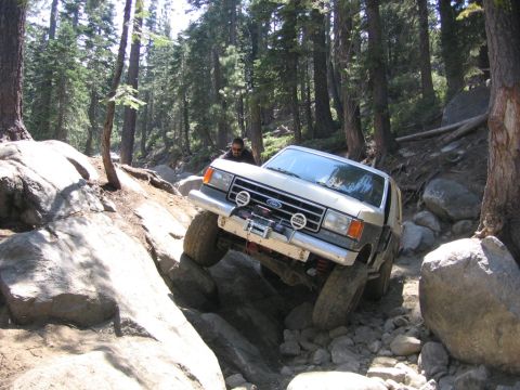 1989 Ford Bronco - A Ford Bronco navigates a challenging rocky terrain with a driver visible inside.