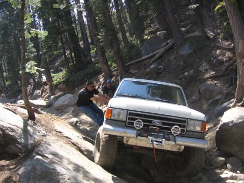 1989 Ford Bronco - A white 1989 Ford Bronco is seen off-roading on a rocky trail with two people assisting.