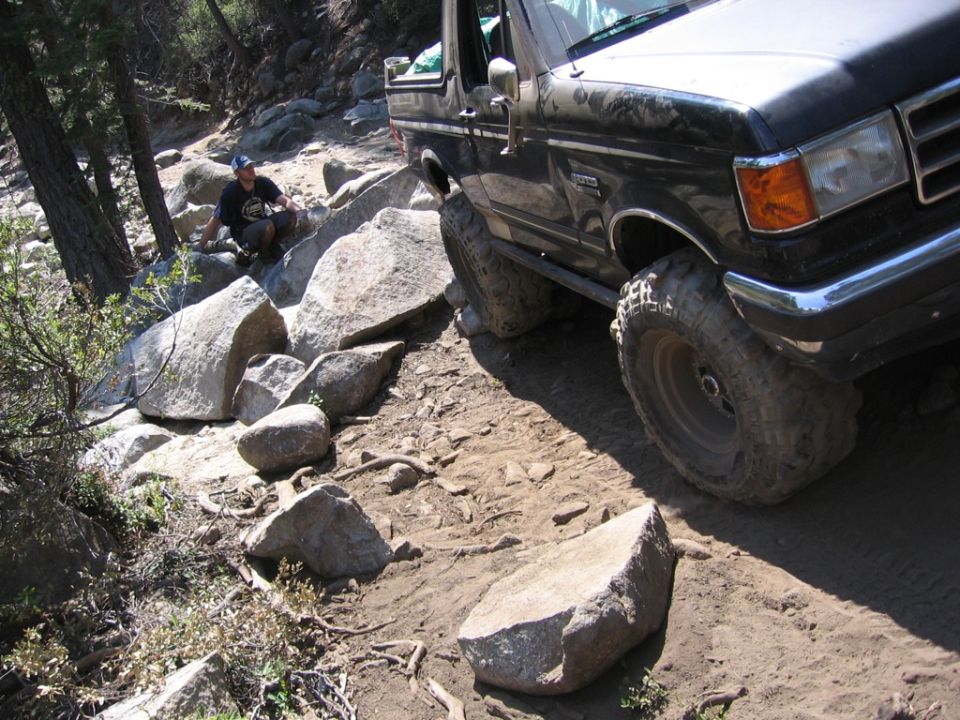 Black 1987 Ford Bronco navigating a rocky, dirt trail with large boulders
