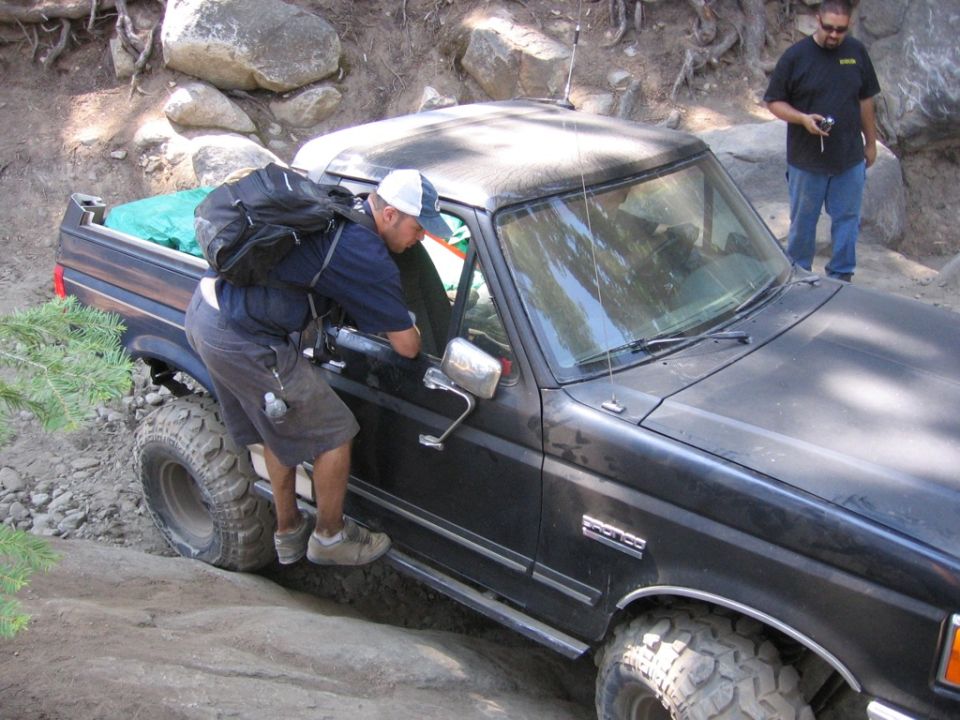 1989 Ford Bronco with large tires on rocky terrain, driver leaning in
