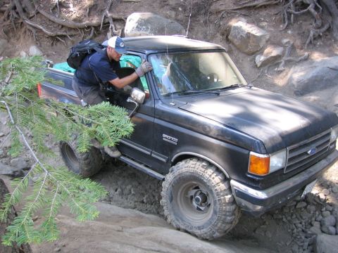 1989 Ford Bronco - A man climbs into a black 1989 Ford Bronco as it maneuvers over a rocky trail.