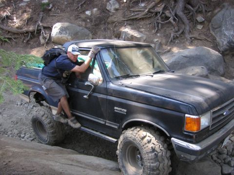 1989 Ford Bronco - A man climbs into a black Ford Bronco navigating a rough, rocky terrain.