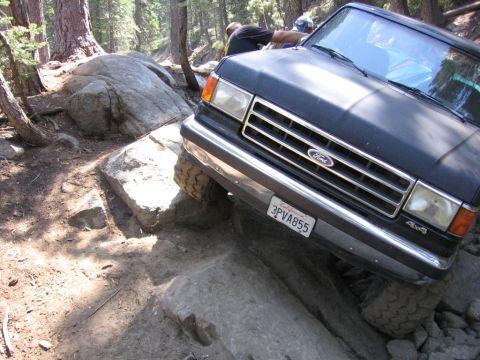 1989 Ford Bronco - A 1989 Ford Bronco is shown navigating a difficult rocky trail in a wooded area.