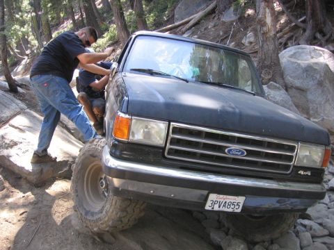 1989 Ford Bronco - Ford Bronco navigating difficult rocky terrain with assistance from passengers.