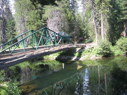 1989 Ford Bronco - A green SUV drives across a narrow bridge in a wooded area with a creek below.