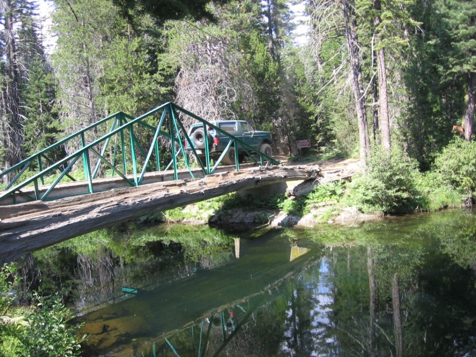 Green SUV crossing a wooden bridge over a creek in a forest