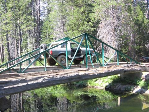 1989 Ford Bronco - 1989 Ford Bronco navigating a rustic wooden bridge in a forest setting.