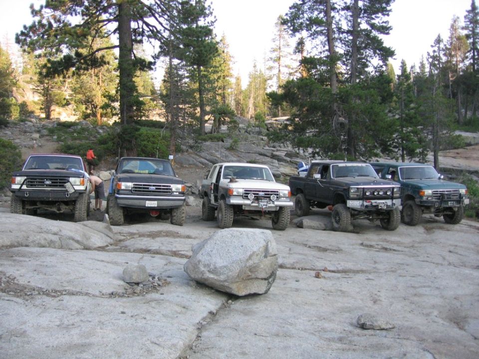 Five 1989 Ford Broncos parked on rocks in a forest