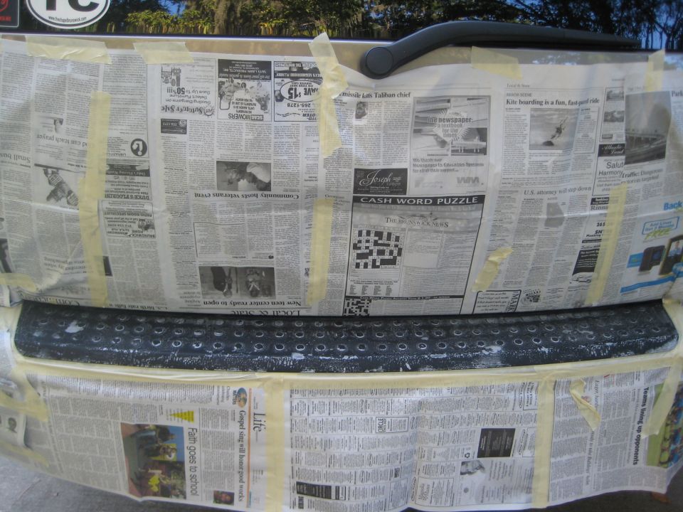 Rear bumper step pad exposed for refinishing, surrounding tailgate masked with newspaper and tape