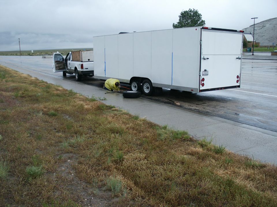 White 2000 Ford F-250 pickup truck with driver's door open, towing a large white enclosed trailer on a wet road