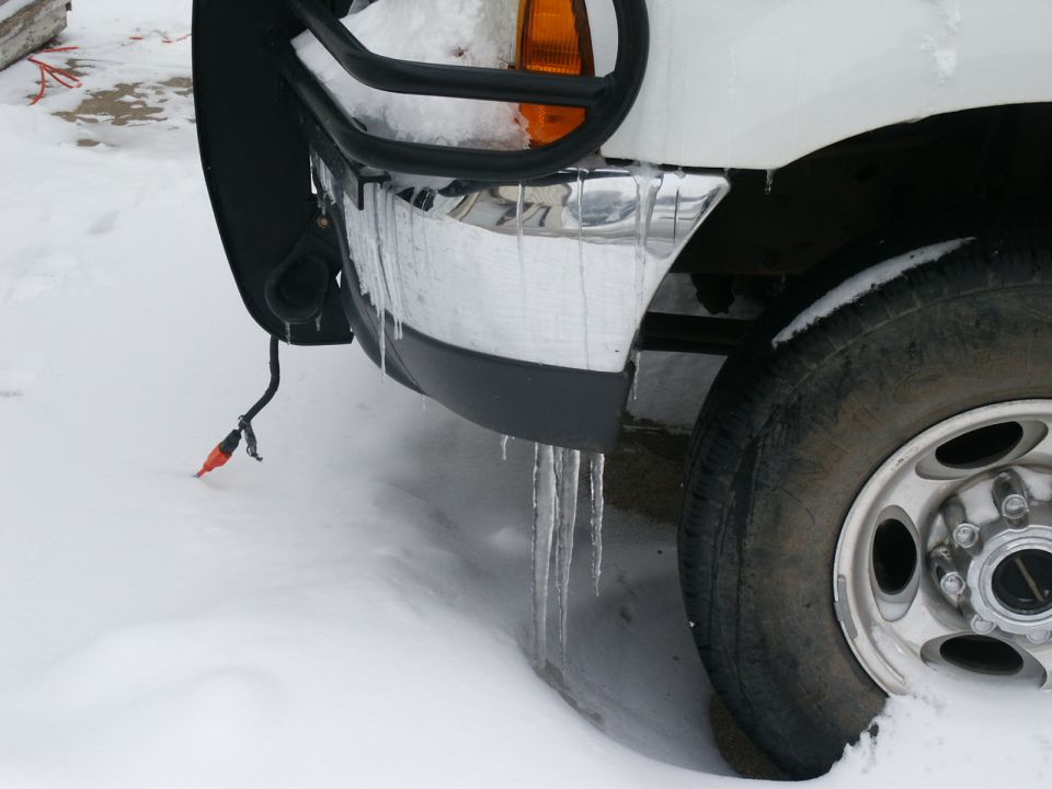 2000 Ford F-250 front bumper with chrome and black trim, icicles hanging from the bumper and grille guard in the snow