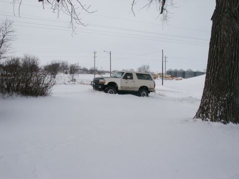 1990 Ford Bronco - A white Ford Bronco is stuck in a snow-covered field with its front end buried.
