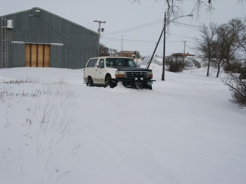 1990 Ford Bronco - A white Bronco with a black hood is stuck in deep snow near a large building.