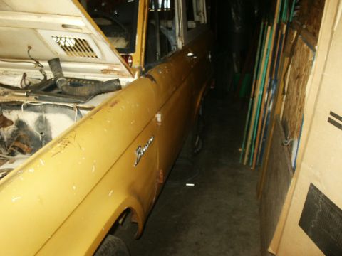 1966 Ford Bronco - The side of a yellow Ford Bronco is visible, with the hood open, in a dimly lit indoor space.