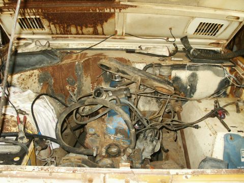 1966 Ford Bronco - The engine bay of a heavily rusted vehicle, with visible engine components, hoses, and wiring harnesses.