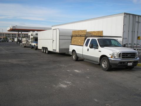 1989 Ford F-350 - A white Ford F-350 truck is parked next to a large white trailer, with lumber secured on a rack above the truck bed.