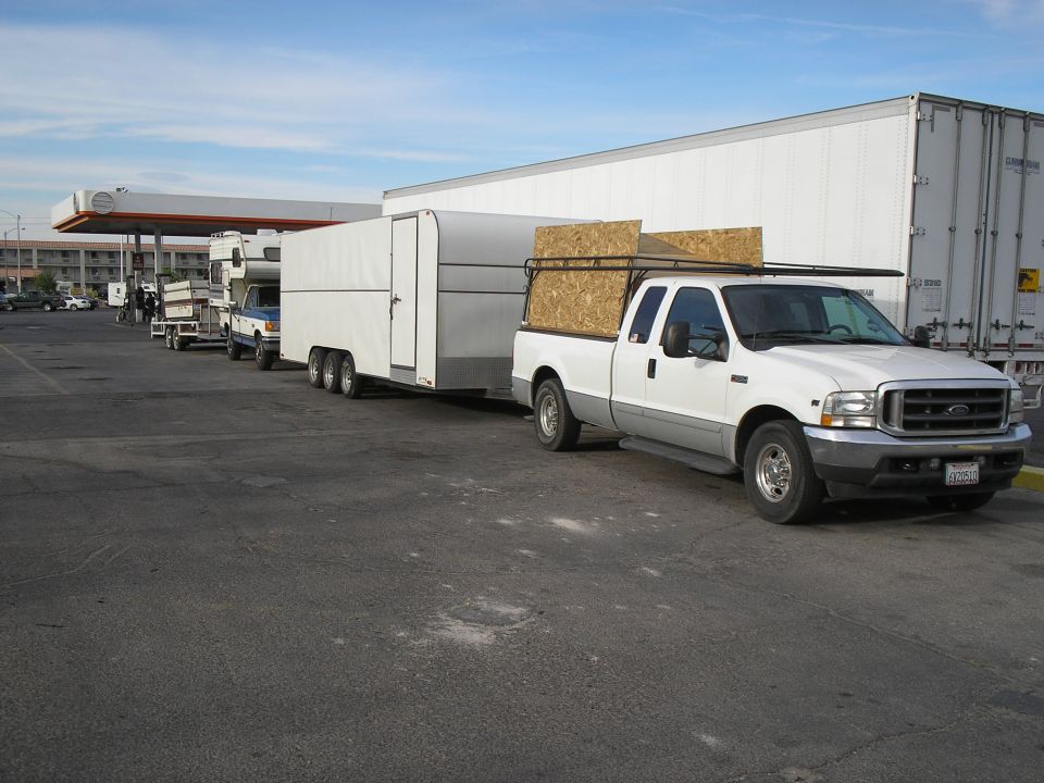 White Ford Super Duty extended cab towing an enclosed tri-axle trailer at a truck stop