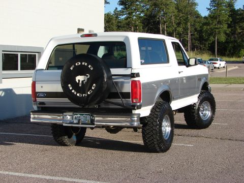 1995 Ford Bronco - Lifted 1995 Ford Bronco features a two-tone paint scheme and a spare tire mounted on the rear tailgate.