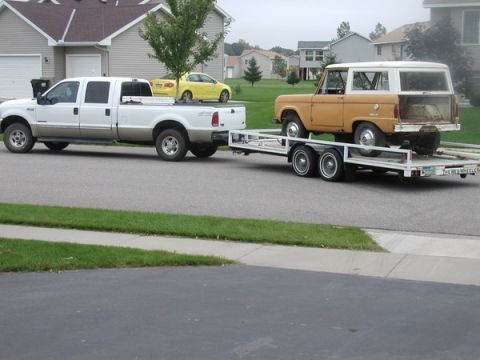 2000 Ford F-250 - Ford F-250 Super Duty tows a classic Ford Bronco on a trailer down a suburban street.