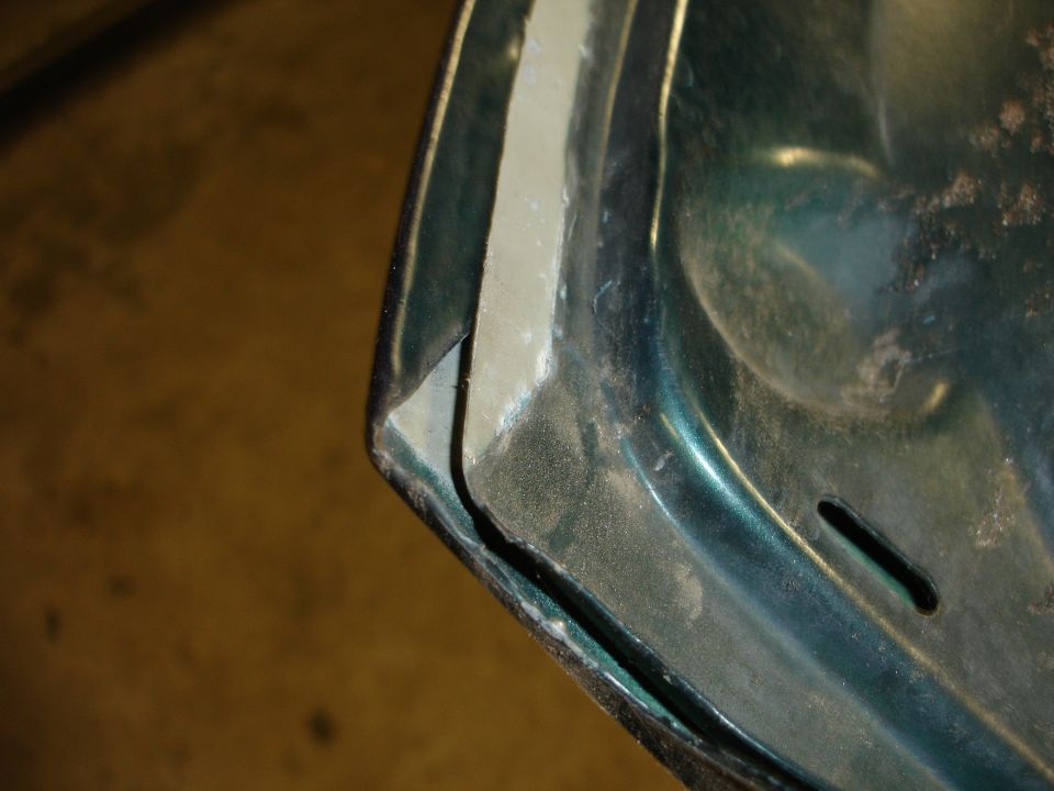 Close-up of a teal-green painted sheet-metal panel corner with a slotted hole