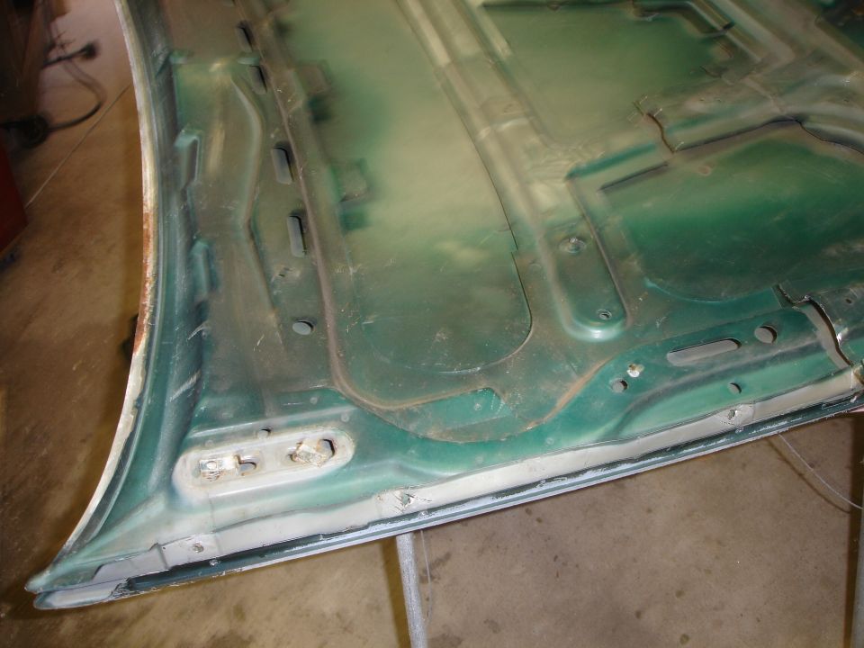 Underside of a removed car hood in green primer showing stamped inner bracing