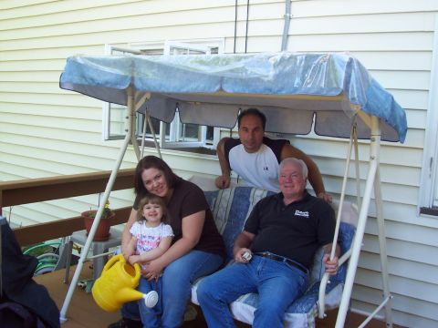 2000 Ford Crown Victoria - A family enjoys a sunny day on a porch swing, with a young child holding a yellow watering can.