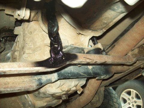 1985 Ford Bronco - A black chain is bolted to a crossmember on the underbody of a vehicle, with other suspension components visible.