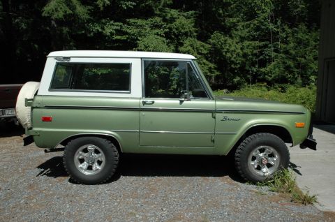 1973 Ford Bronco - A side view of a classic green Ford Bronco with a white roof, parked on a gravel driveway.