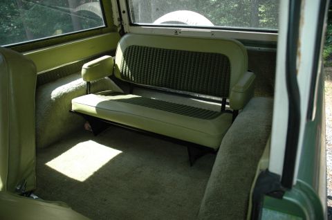1973 Ford Bronco - The interior of a vehicle shows a green bench seat and carpeted floor with sunlight streaming in.
