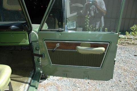 1973 Ford Bronco - Interior door panel of a 1973 Ford Bronco, showing green paint, wood grain accents, and a light green armrest.