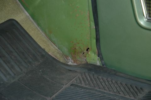 1973 Ford Bronco - Interior view shows rust damage on a green panel next to a black floor mat.