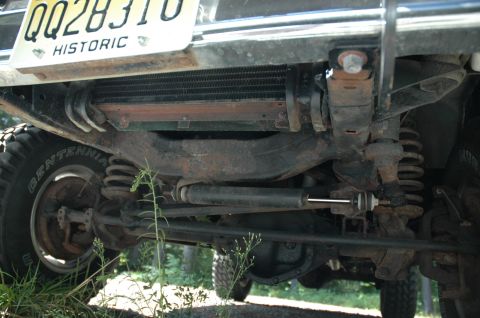 1973 Ford Bronco - The underside of a vehicle is visible, including the front axle, springs, and a radiator. A license plate is mounted above.