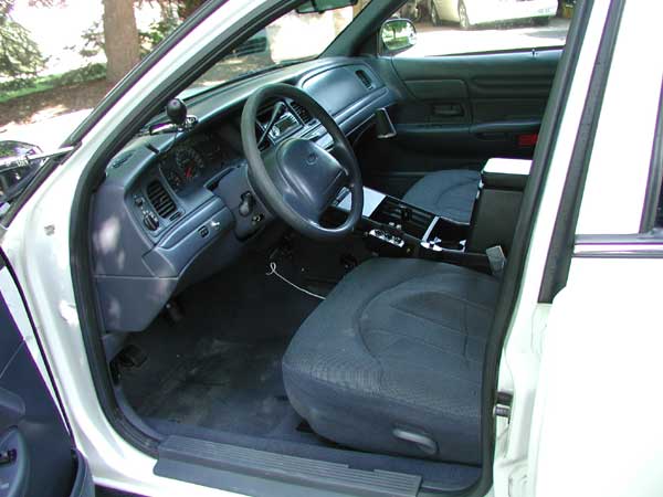 Driver's side interior of white Crown Victoria with gray dash, cloth seat, spotlight handle and center console equipment.
