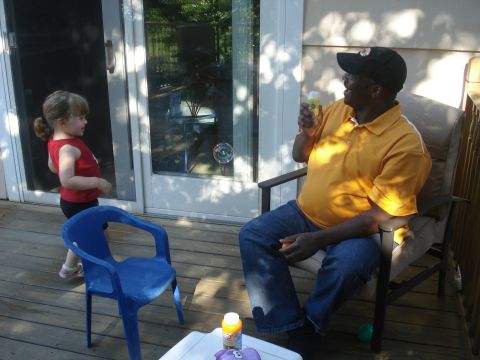 2000 Ford Crown Victoria - A man sits on a deck chair holding a bottle, while a child stands nearby, looking towards a glass door.