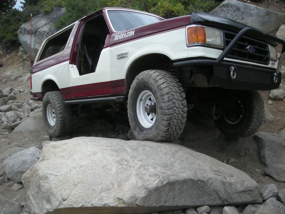 Maroon and white 1991 Ford Bronco climbing large rocks