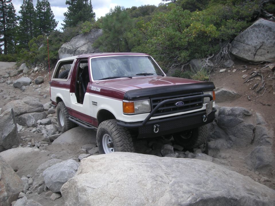 1991 Ford Bronco navigating a rocky trail, two-tone red and white paint, aftermarket front bumper