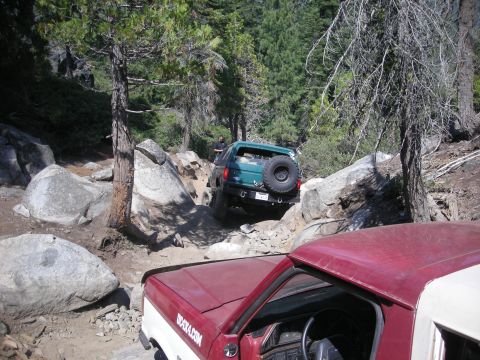 1991 Ford Bronco - A green SUV tackles a challenging rocky trail, with another vehicle visible in the foreground.