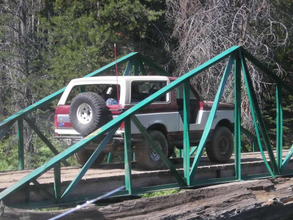 1991 Ford Bronco on a green metal truss bridge, trees in background