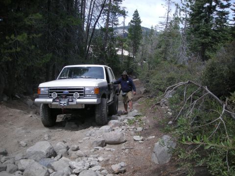 1991 Ford Bronco - A man walks next to a Ford Bronco navigating a rocky, wooded path.
